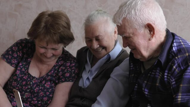 Mature woman and her parents of retirement age making video call using the mobile phone. Elderly woman and man and their adult daughter have a video conference via smartphone 