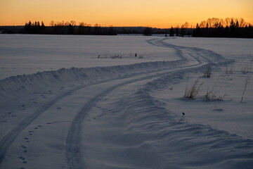 Winter road through a snow-covered field on the background of sunset.