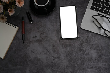 Top view smart phone, laptop computer and notepad on dark stone textured background.