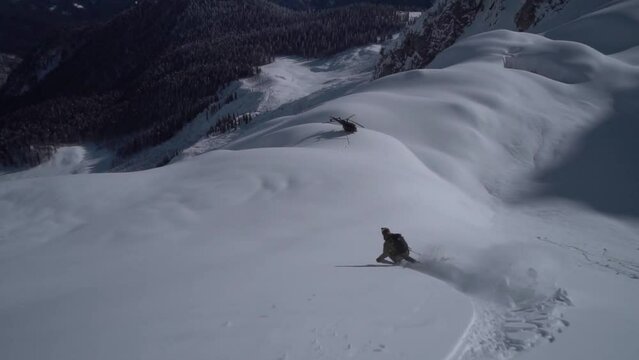 expert skier skiing down powder snow slope to helicopter