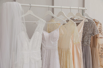 Fototapeta na wymiar Hangers with different beautiful dresses and wedding veil on rack in atelier