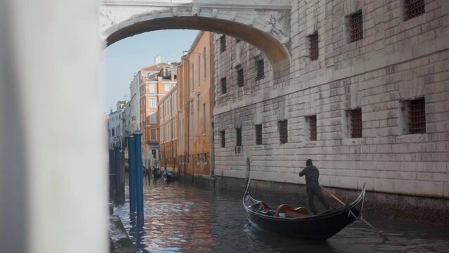 A skipper advances his gondola by moving his large wooden paddle through the water in the historic center of Venice with the Bridge of Sights on a sunny day. Close up shot