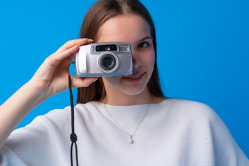 Young caucasian woman holding vintage camera on blue background in studio