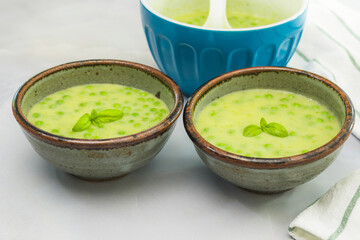 Creamy celery soup with green peas and fresh basil close up in bowls on light grey marble background