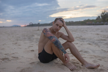 Full-length portrait of handsome caucasian man sitting on the sand on the beach