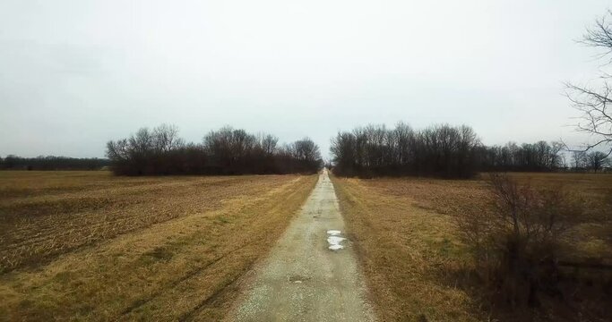 Drone fly above lonely remote desolated road in countryside driving through plowed agricultural field 
