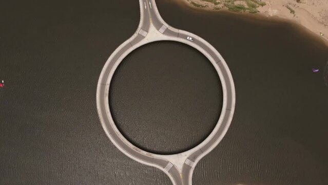 White car driving on circular bridge of Garzon lagoon in Uruguay. Aerial top-down orbiting