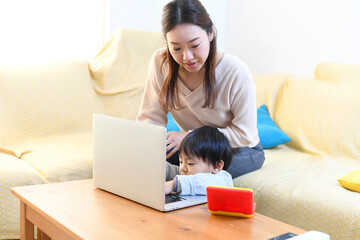 ノートパソコンを操作するお母さんと小さいアジア人の男の子
