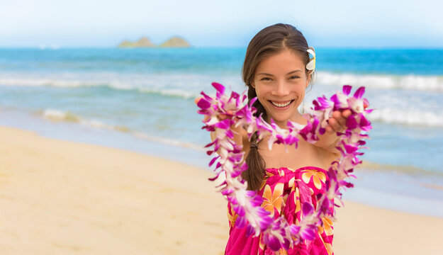 Hawaiian lei girl giving flowers as welcome to Hawaii beach travel vacation destination. Happy Asian woman hula dancer smiling portrait.