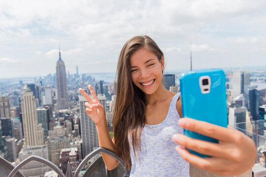 Phone selfie in New York tourist woman taking mobile picture at skyline. Asian girl holding smartphone for self-portrait photo with view of Manhattan skyscrapers during summer travel vacation.