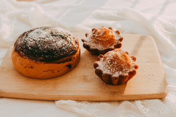 cupcakes and a bun with chocolate sprinkled with powdered sugar on a wooden background
