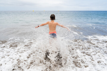 A teenager is standing on the sandy shore of the ocean.