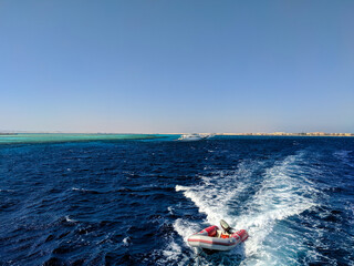Obraz premium Hurghada, Egypt - October 1, 2021: Beautiful view of the bright red sea. Rubber boat tied to a yacht floats on the waves. Copy space.