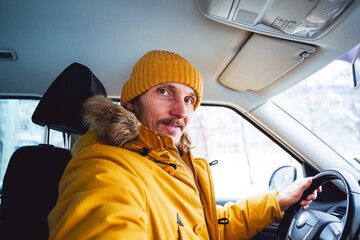 attractive man behind the wheel of a car. The guy has bright clothes and a happy face. Drive in winter. Moving around the city by car. Passenger seat