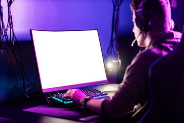 A focused gamer playing video games on computer in gaming room.