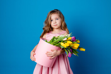 little girl in a pink dress holds a pink hatbox with a bouquet of tulips in her hands. fresh flowers. International Women's Day. space for text. High quality photo