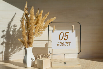 august 5. 5th day of month, calendar date. White vase with dead wood next to the numbers 2022 and stand with an empty sheet of paper on table. Concept of day of year, time planner, summer month