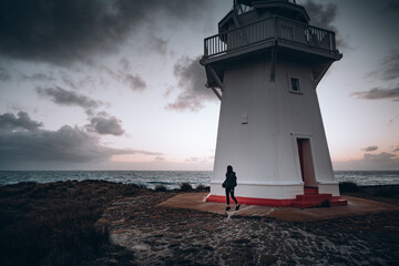Girl standing next to a lighthouse at sunset