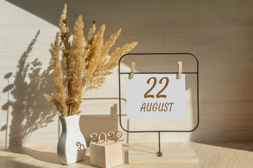 august 22. 22th day of month, calendar date. White vase with dead wood next to the numbers 2022 and stand with an empty sheet of paper on table. Concept of day of year, time planner, summer month