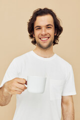 Attractive man with a white mug in his hands emotions posing beige background