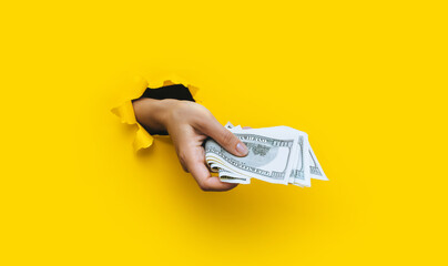 A female hand appears in the hole in torn yellow paper and squeezes several hundred-dollar bills....