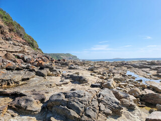 Fototapeta na wymiar Rock Platform with rock pools at Hams Beach Newcastle Australia. With a blue sky and a few clouds