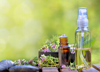 bottles of essential oil and flowers of aromatic herb on a table and on green background