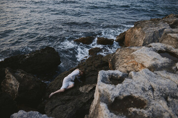 sensual woman in a secluded spot on a wild rocky coast in a white dress view from above