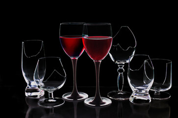 Two glasses with red wine surrounded by broken glasses on a black background.