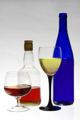 A glass of white wine and a bottle, a glass of whiskey and a bottle. 