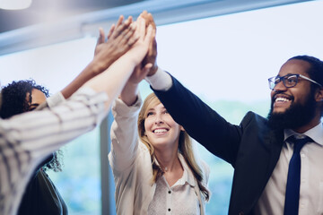 We did it, together. Low angle shot of a group of young businesspeople high fiving in celebration while standing in their office.