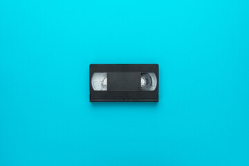 Retro video tape over turquoise blue background with central composition. Old black videocassette...