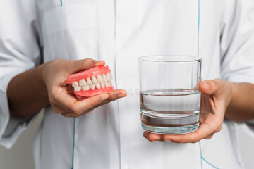 Prosthesis in a glass with a solution. Dental prosthesis care. Full removable plastic denture of...