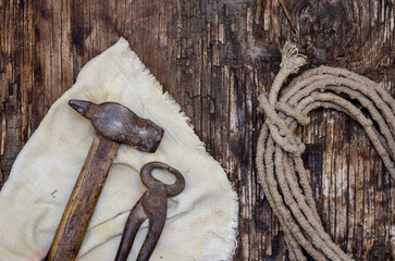 An old hand tool, a roll of rope, and a tattered rag on a dark wooden background.