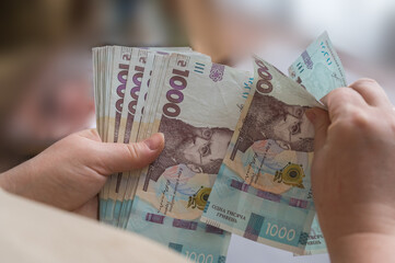 A woman's hands are holding a bundle of Ukrainian hryvnias. Banknotes in denominations of 1000 hryvnia. Close-up. Selective focus. - obrazy, fototapety, plakaty
