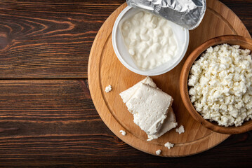 Cottage cheese, granular, crumbly and in briquette on dark wooden background.