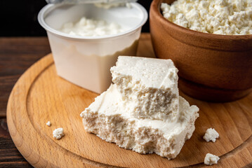 Cottage cheese, granular, crumbly and in briquette on dark wooden background.