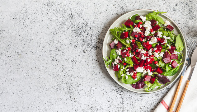 Arugula, Beet and cheese salad with pomegranate and dressing on plate on grey stone kitchen table background, place for text, top view