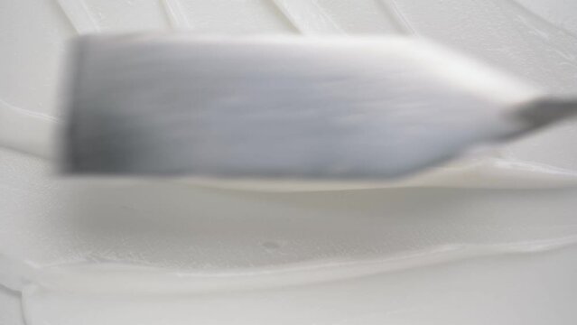 Making strokes of white body cream with small spatula upper macro view. Salon cosmetic remedy for professional beauty care
