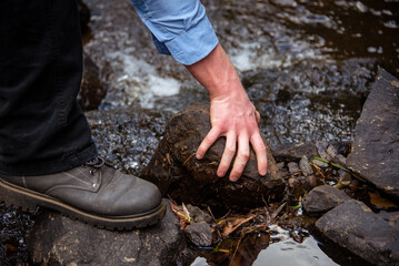 person grabbing a stone near a river