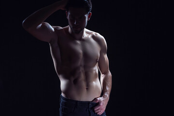 Fototapeta na wymiar Youth Lifestyle. Contrast Portrait of Confident Thinking Caucasian Bodybuilder Athlete Man Posing With Lifted Hand With Naked Torso Against Dark Background.