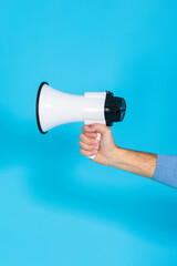 Lifestyle Concepts. Closeup of Hand of Man in Blue Jumper Holding Megaphone Loudspeaker Against Seamless Blue Background.