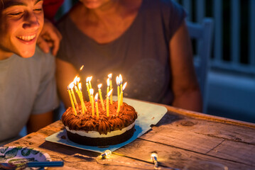 Close up of night party and birthday cake with candles. Young teenager boy and grandfathers enjoy...