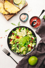 Vegan vegetarian salad with pineapple, arugula, avocado and dried cherry on white stone kitchen table, top view. Healthy eating, clean diet food, weight loss concept