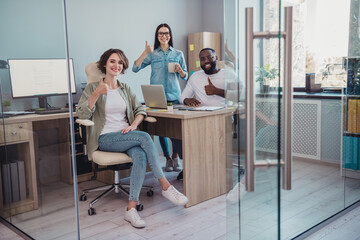 Photo of smiling happy professionals sitting table showing thumb up working devices indoors workshop workplace