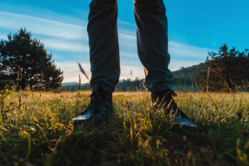 Hiking in the grassland, close up of male feet in leather boots walking through grassy landscape