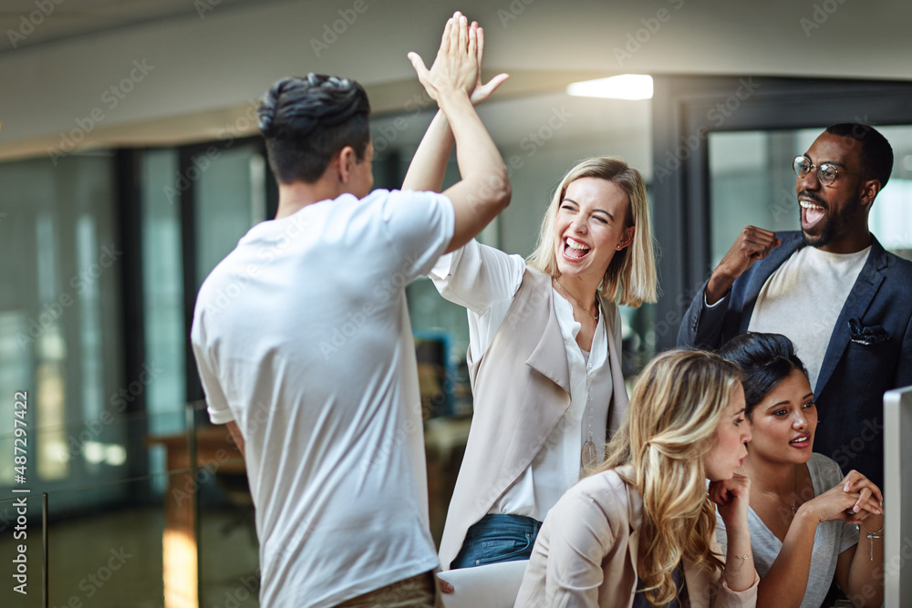 Poster Weve done it again. Shot of a group of colleagues giving each other a high five while using a computer together at work.