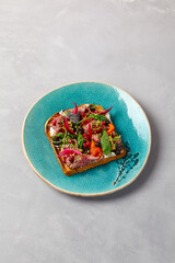 Bruschetta with roast beef, baked paprika and onion on blue ceramic plate. Toast with roast beef in contemporary style. Chef concept bruschetta in modern ceramic dishware. Handmade dinner plate.