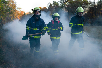 Firefighters men and woman at action, running through smoke to stop fire in forest.