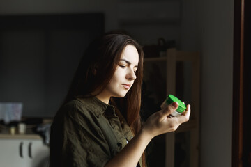 Young dreamy woman reading ingredients on package at home next to window.